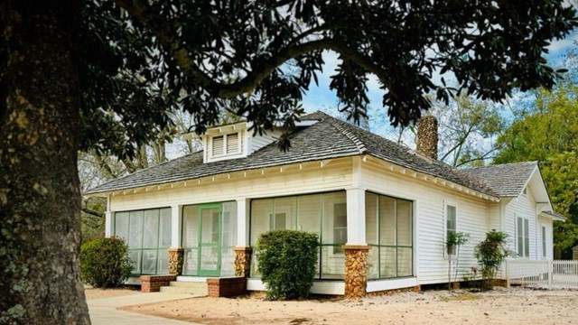 An interpretive sign stands in front of a white wooden building, on either side stand animal pens.